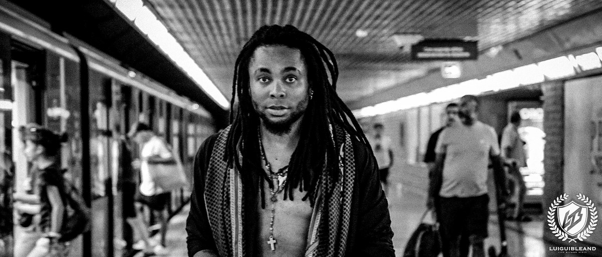 Black-and-white photograph of Luigui Bleand walking alone toward the camera through an underground passage in Milan while other people pass behind him
