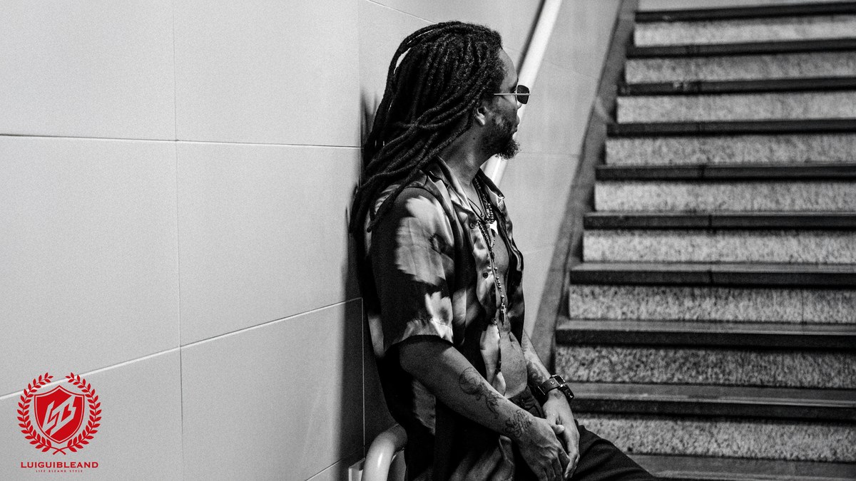 Luigui Bleand beside a staircase, in a black-and-white press photograph with his red logo